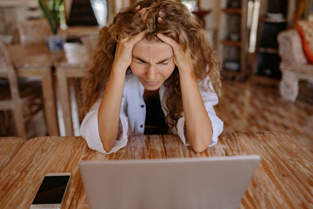 Woman at a laptop. Head in hands, eyes closed in frustration.